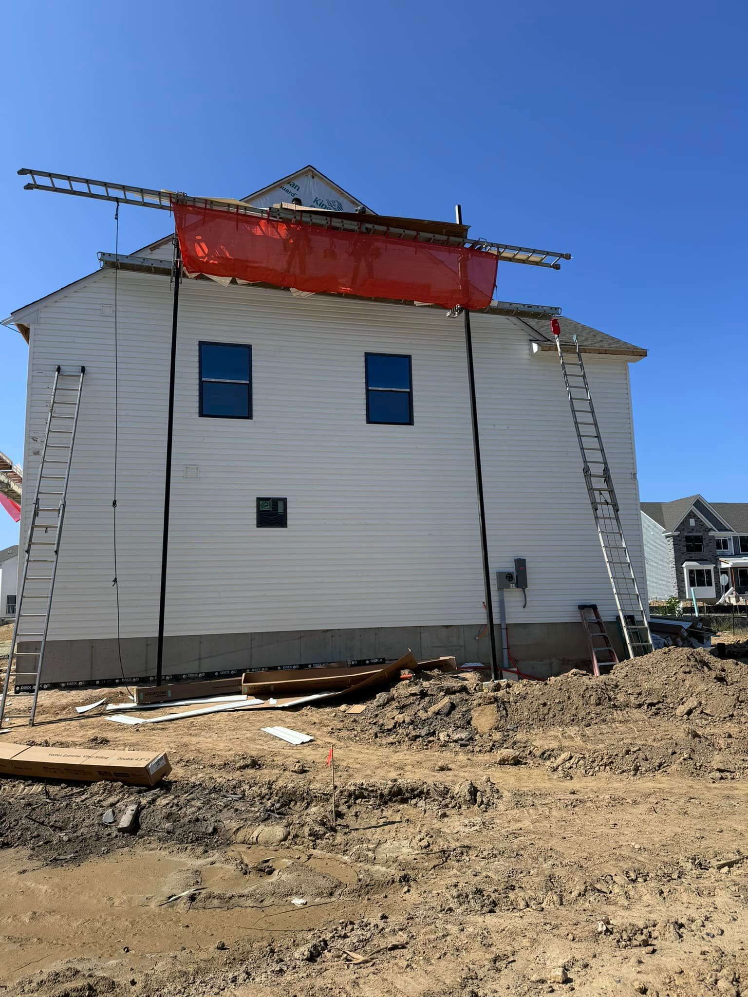 White house under construction with ladders and protective barrier, set on dirt lot, clear blue sky.