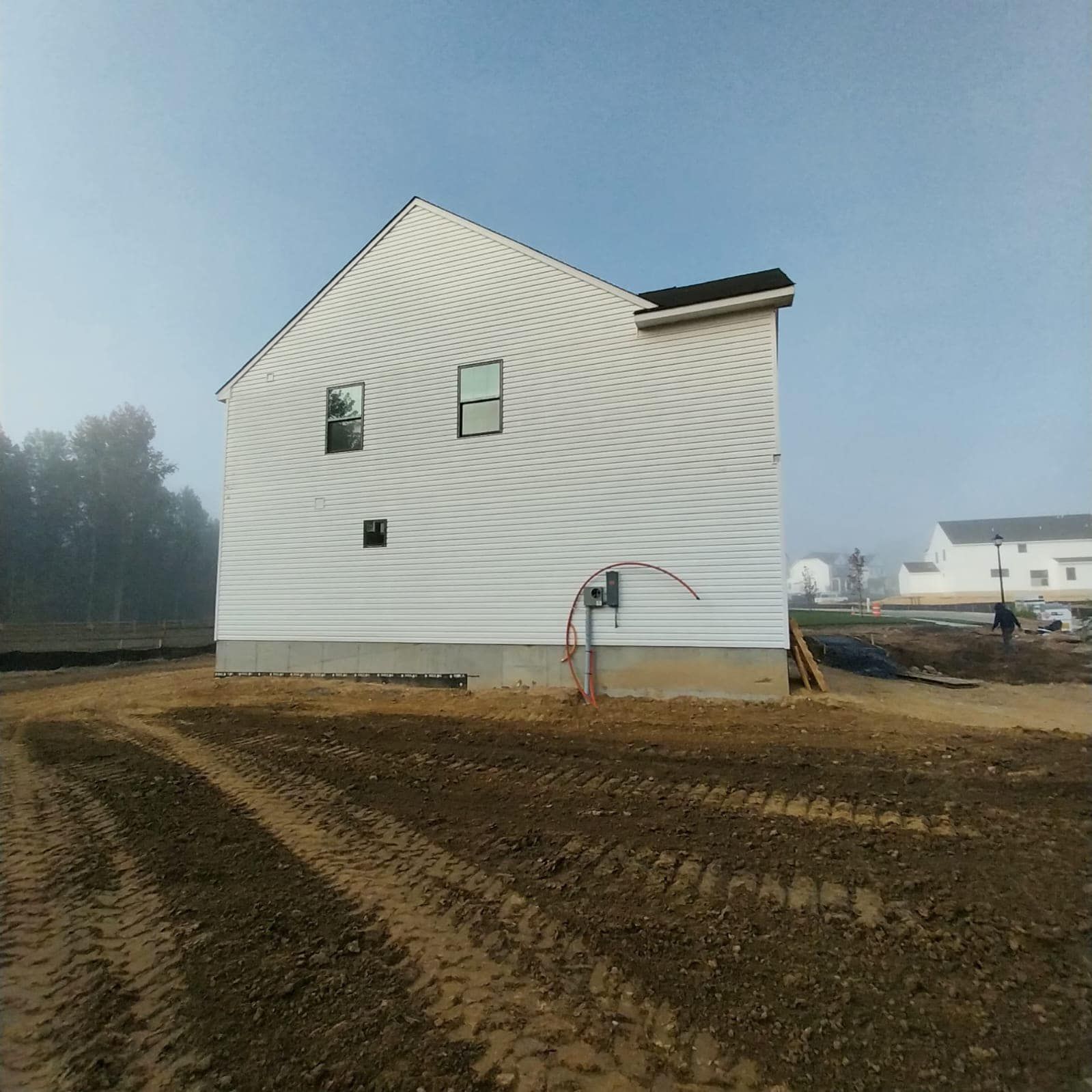 New house under construction with white siding on a muddy lot, misty surroundings.
