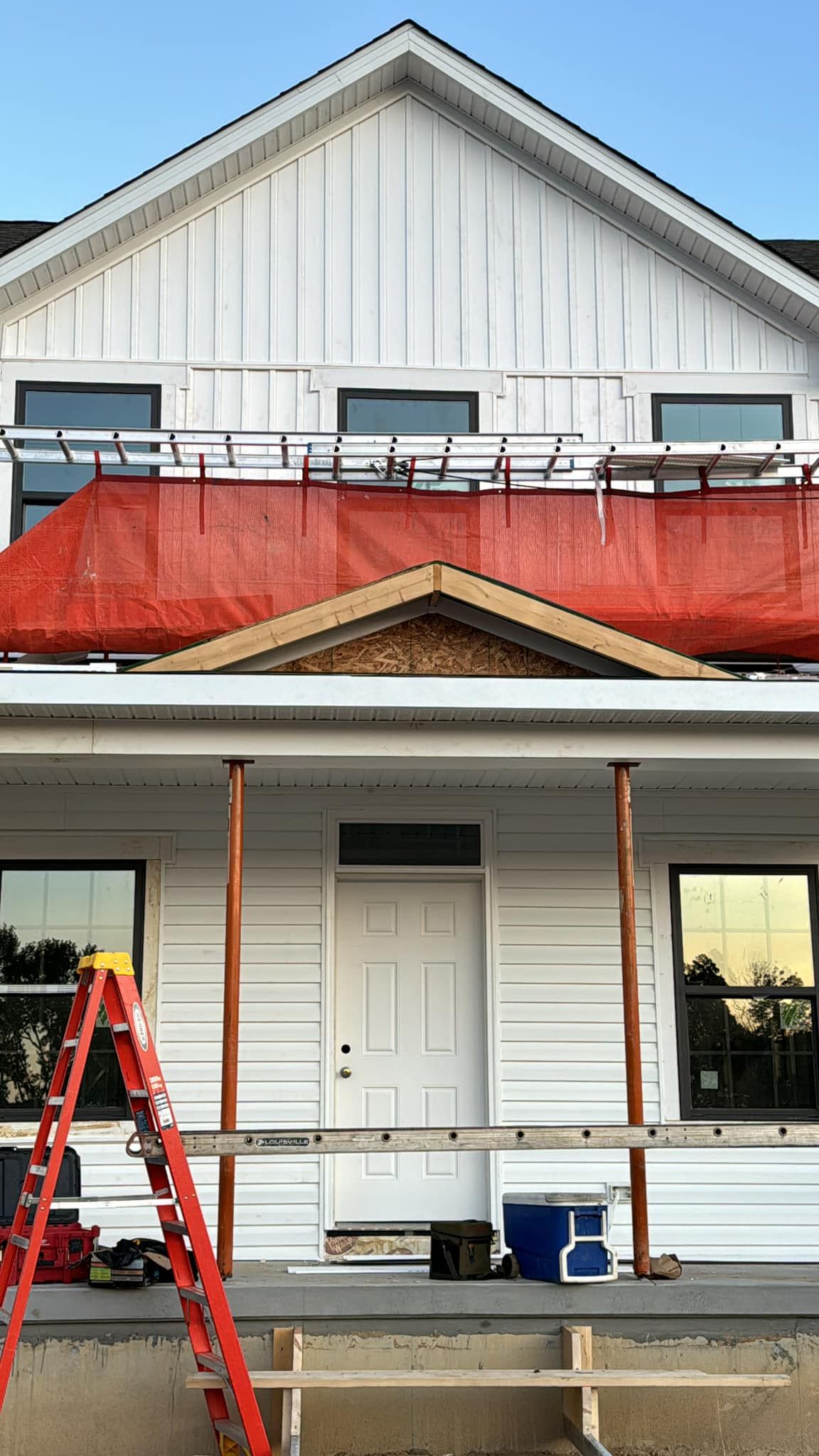 White house under construction, with orange safety netting, ladder, and porch supports.