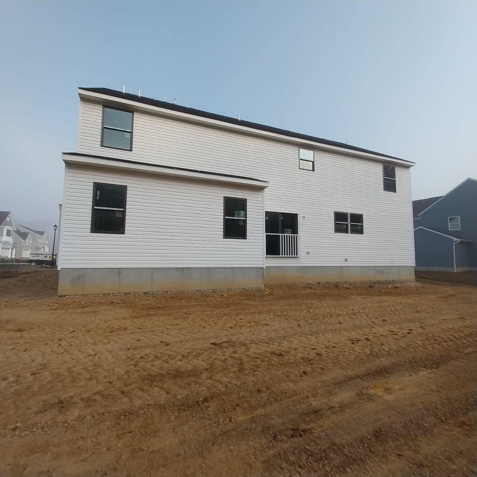 Two-story house under construction with white siding and black windows on a dirt lot.
