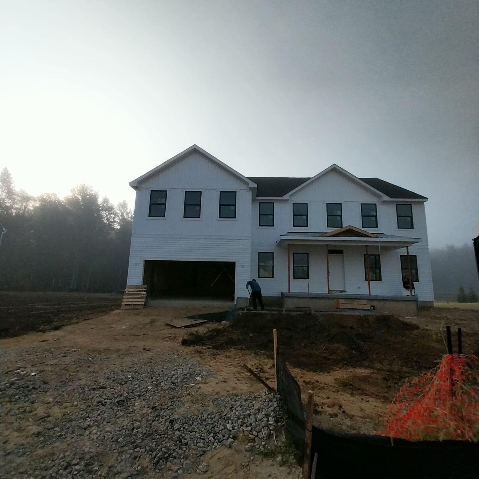 New house under construction, with open garage, in a dirt lot.