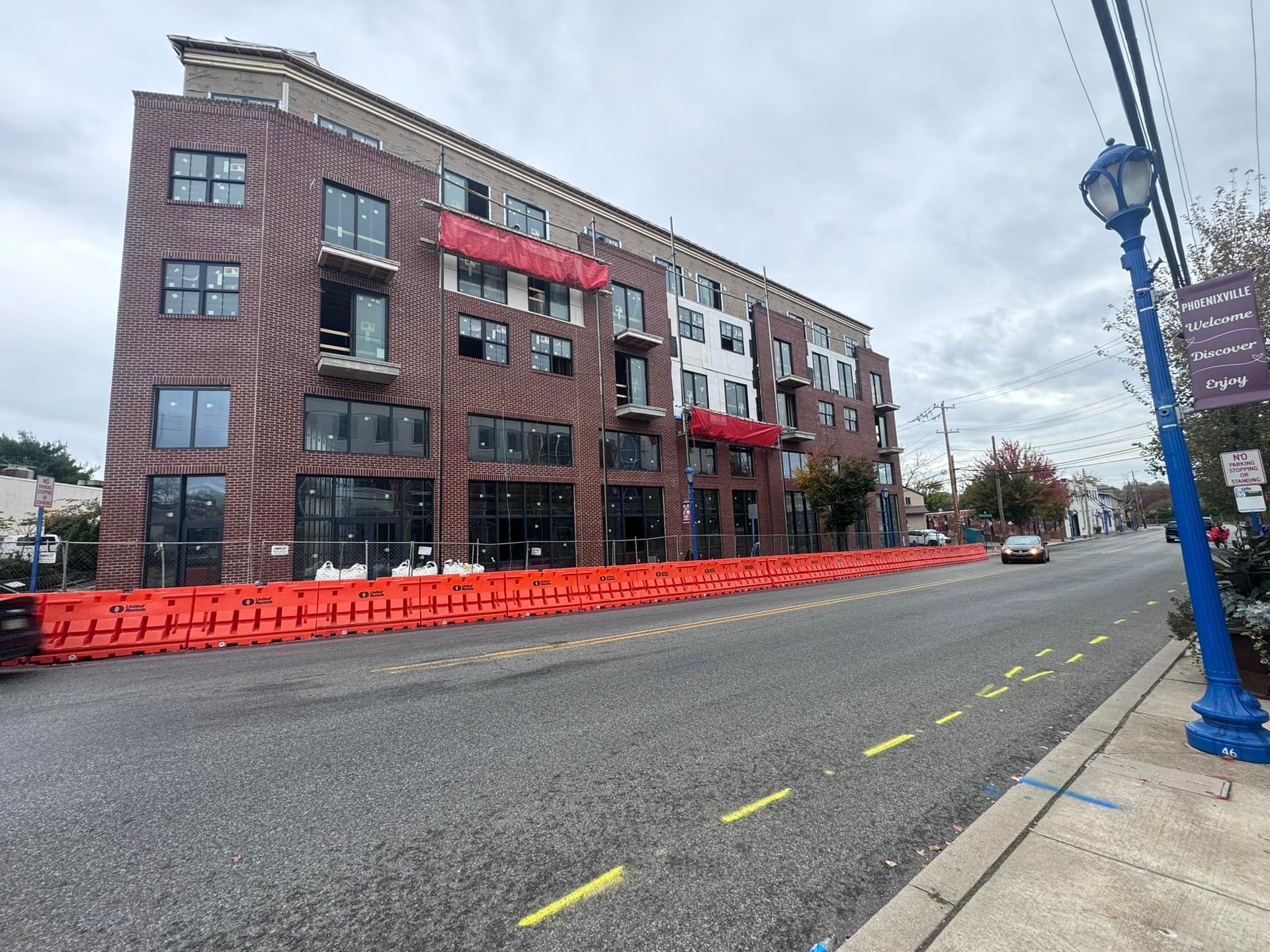 Multi-story brick building under construction with orange barriers lining the street.