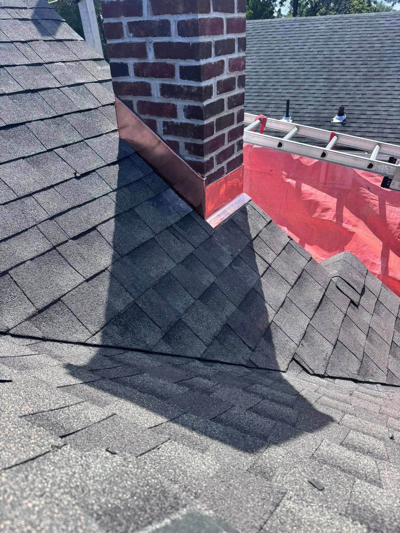 Chimney on a gray shingled roof with copper flashing, and a red underlayment.