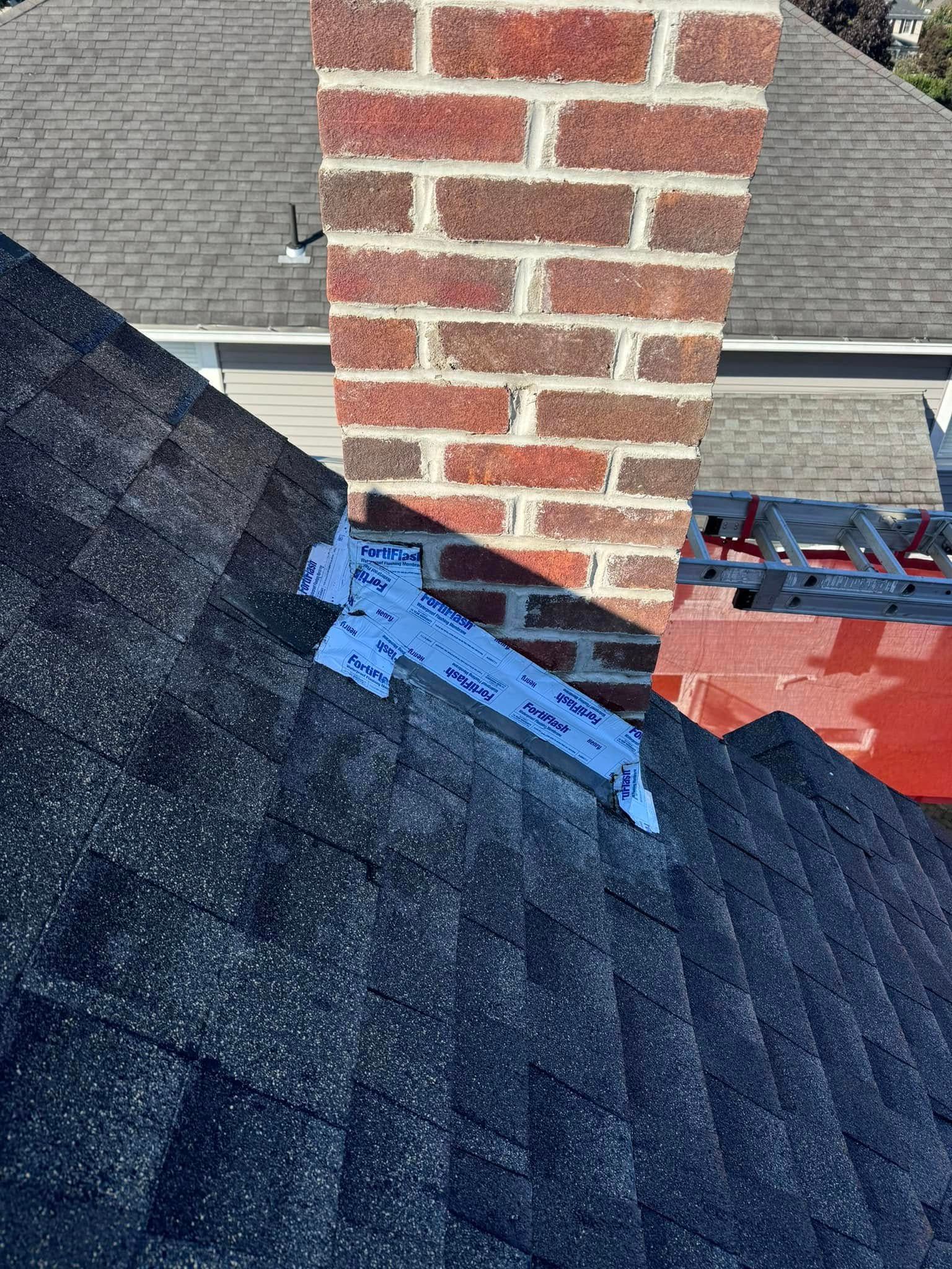 Brick chimney on a dark shingled roof, with blue flashing.
