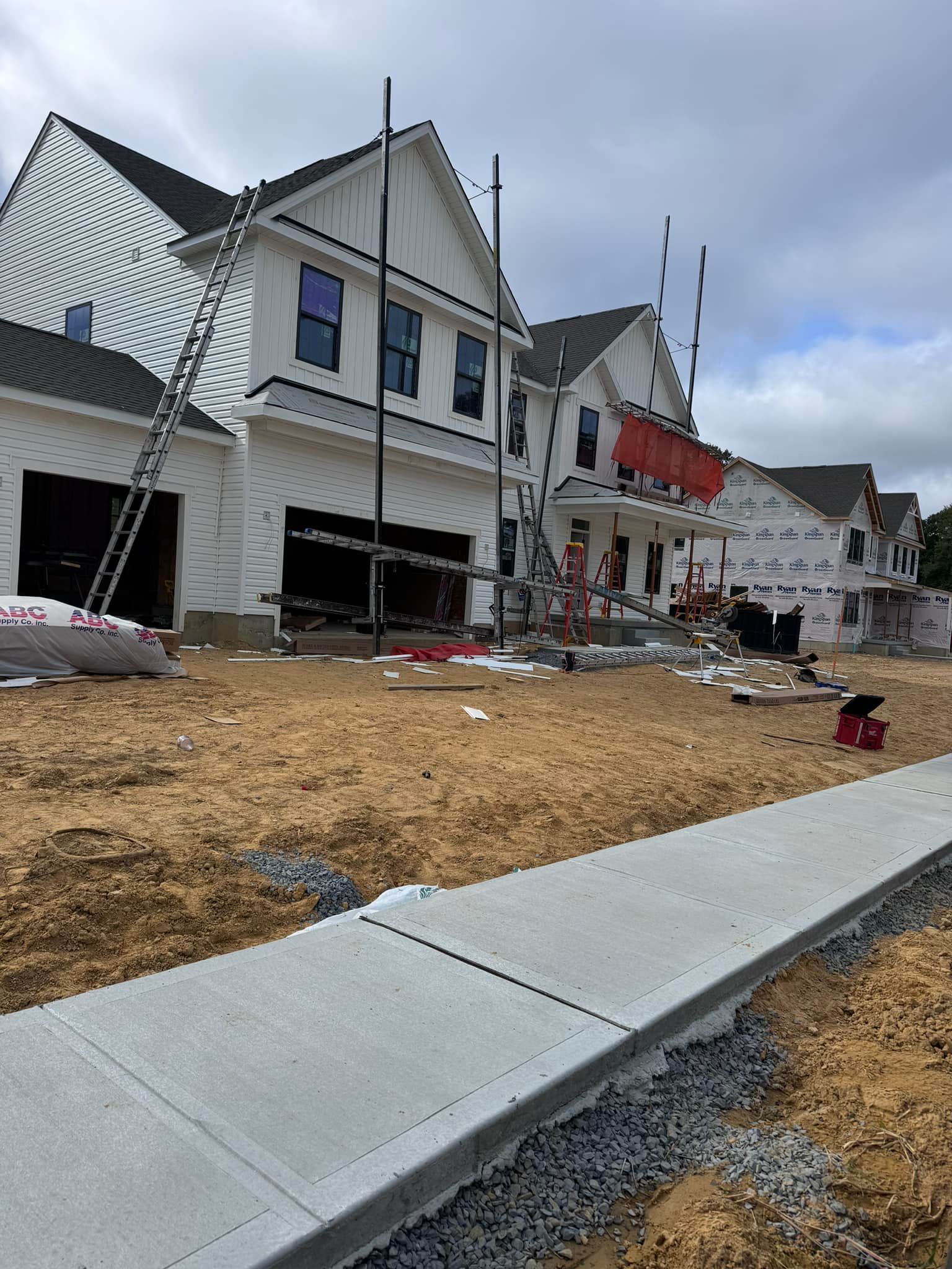 New houses under construction with scaffolding, sidewalk, and dirt lot.