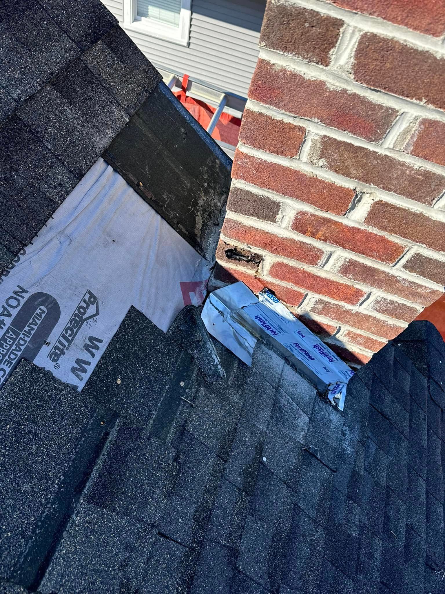 Roof with shingles meeting a brick chimney; flashing and sealant visible.