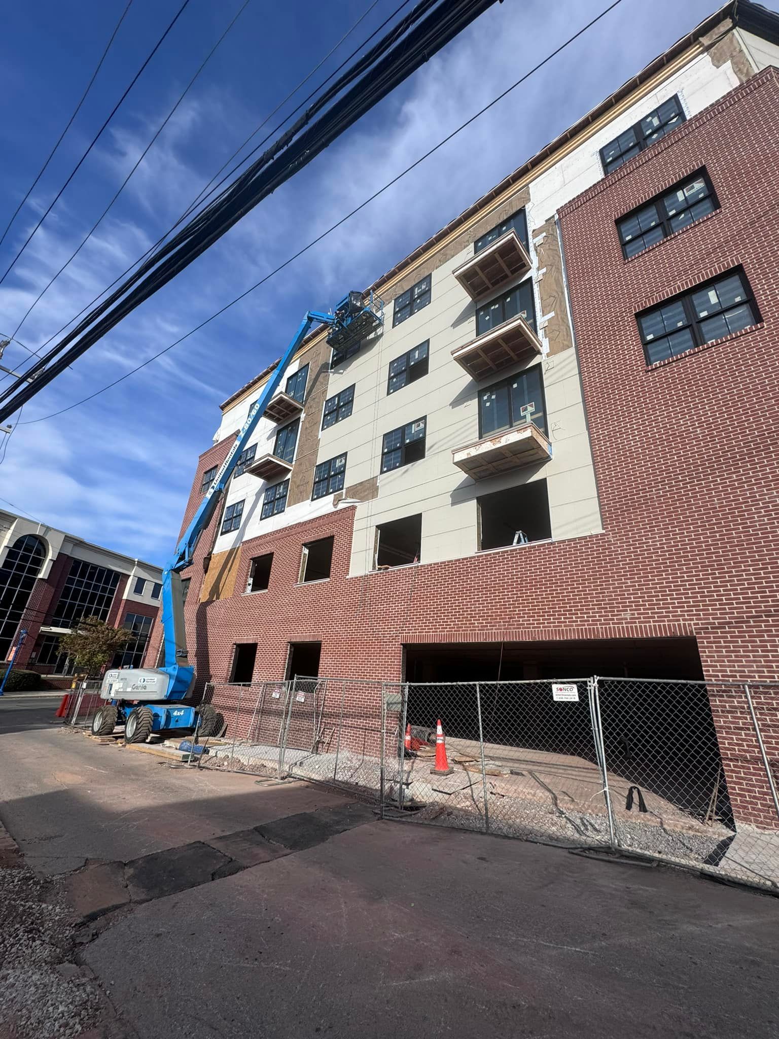 Building under construction; brick and siding exterior; blue lift; cloudy sky.