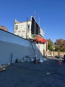 Building exterior under construction; scaffolding, ladder, safety netting, blue sky, debris on ground.