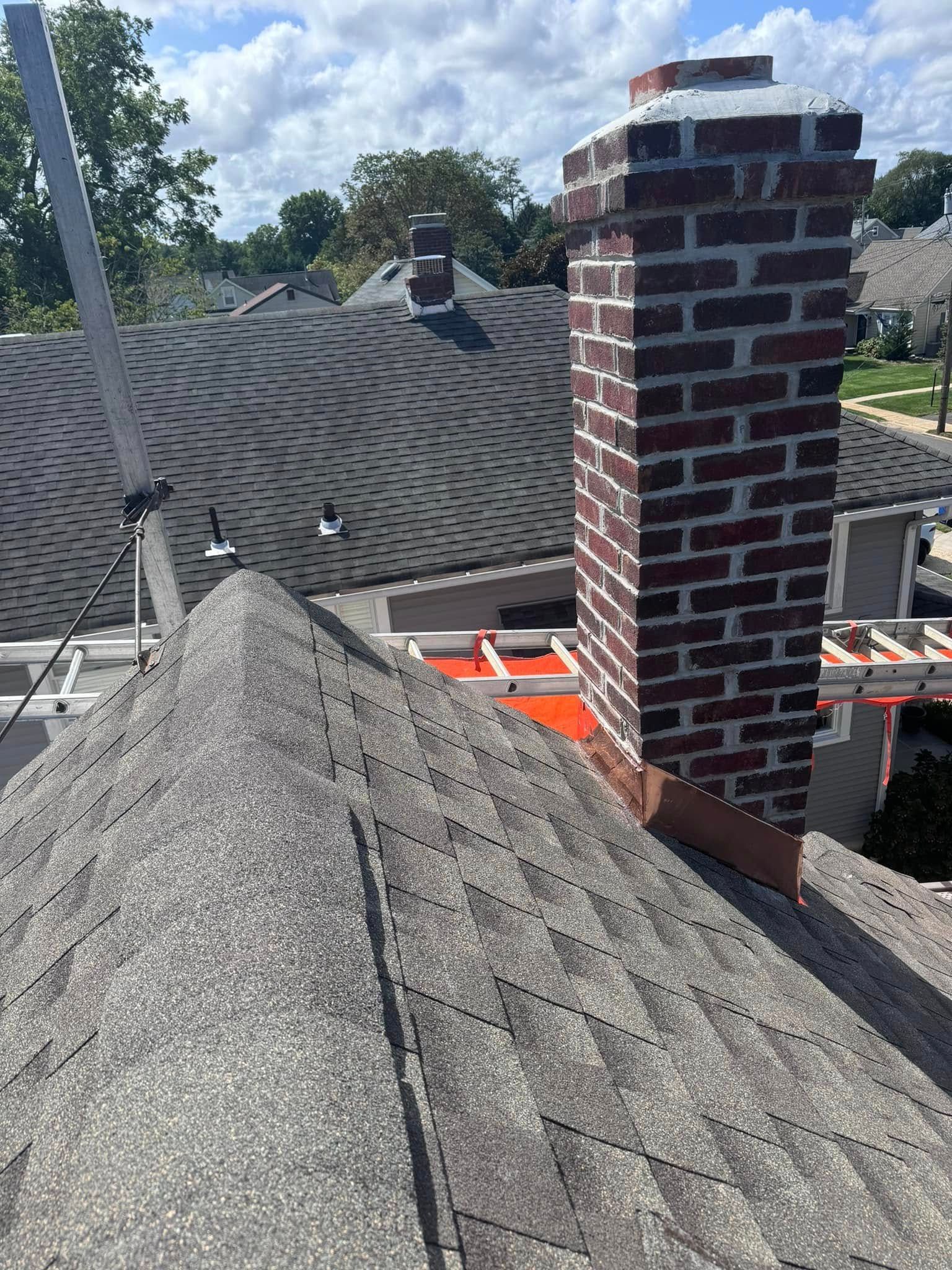 Brick chimney on a gray asphalt shingle roof; metal scaffolding and orange safety rails visible.