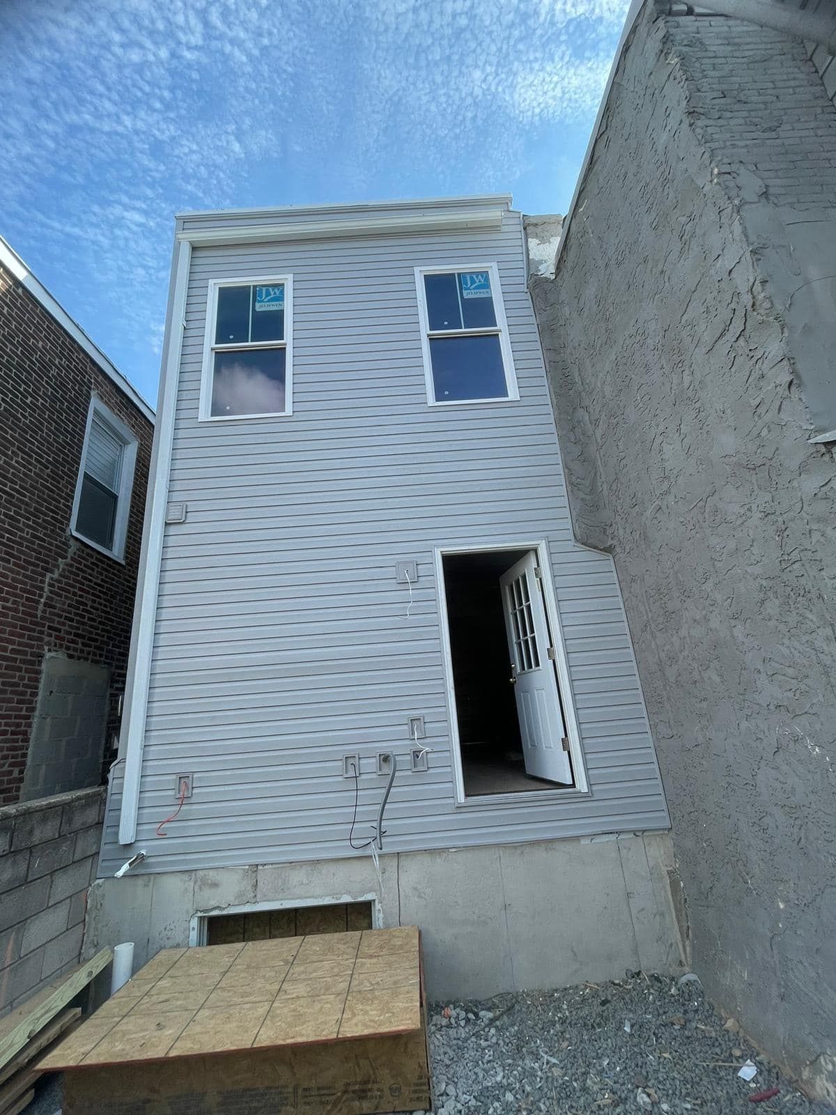 Exterior of a two-story building under construction with gray siding, two windows, and an open doorway.