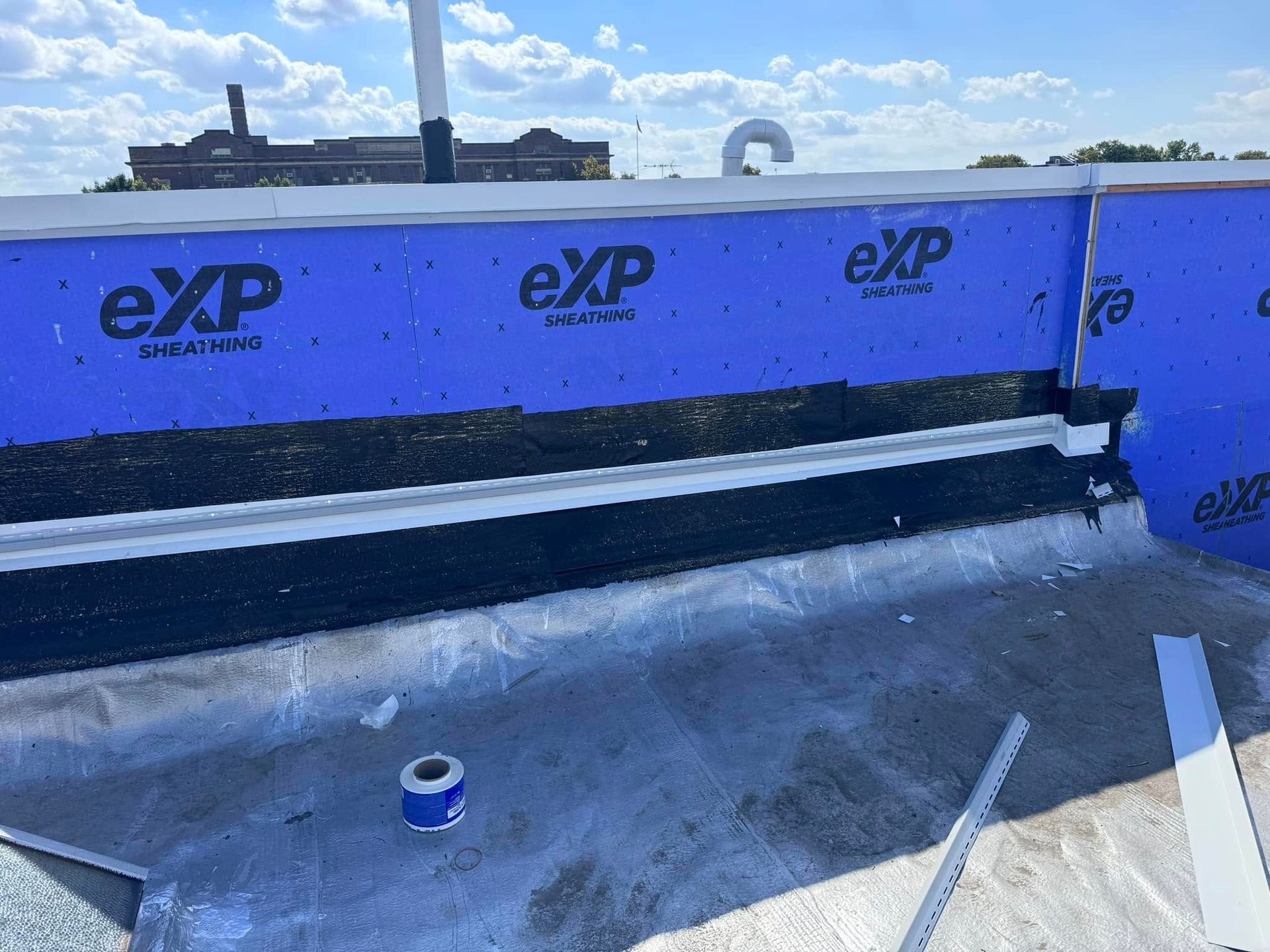 Flat roof construction detail with blue waterproofing, black sealant, and white trim.