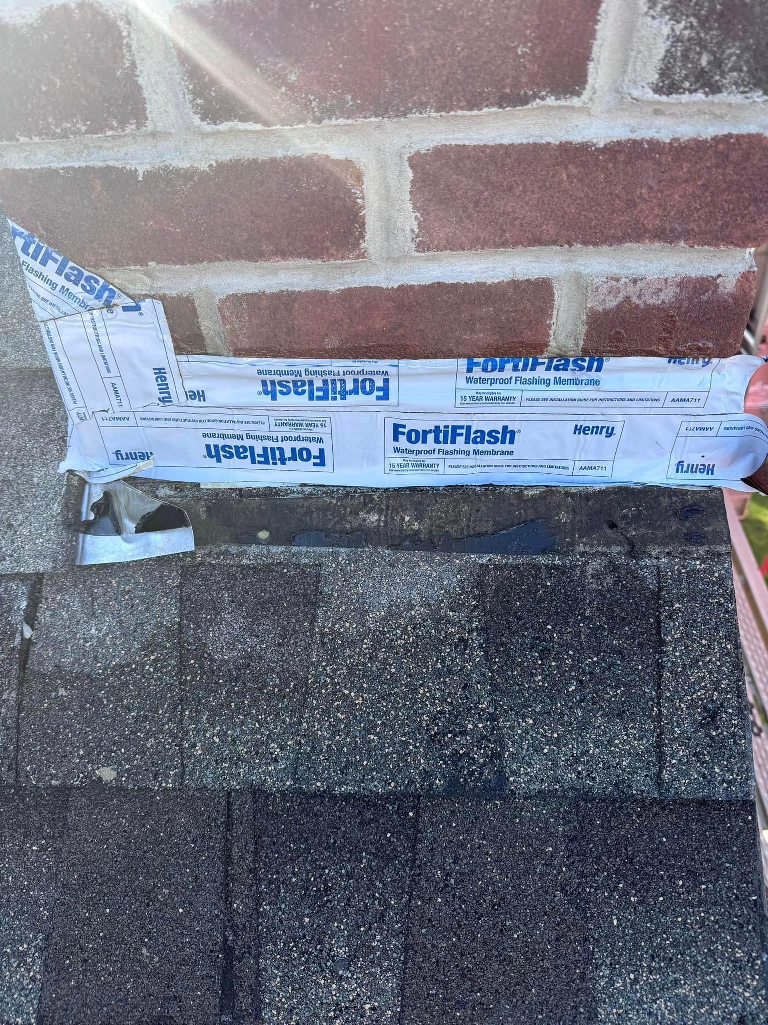 A section of roofing material with flashing tape against a brick wall.