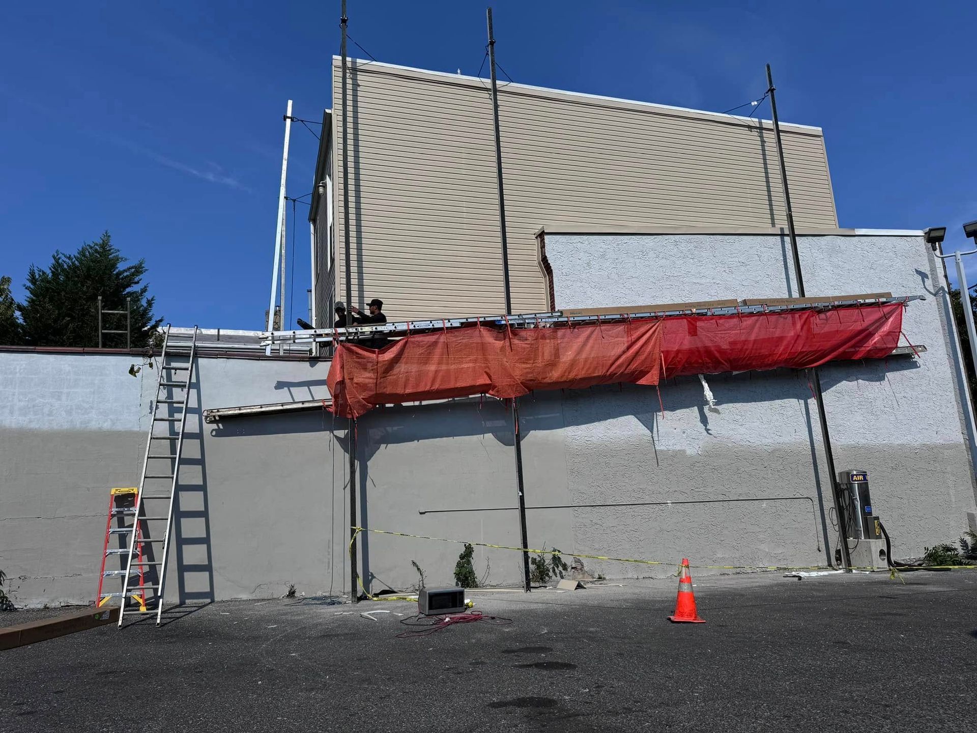 Building exterior under construction with scaffolding, ladder, orange netting, and safety cone.