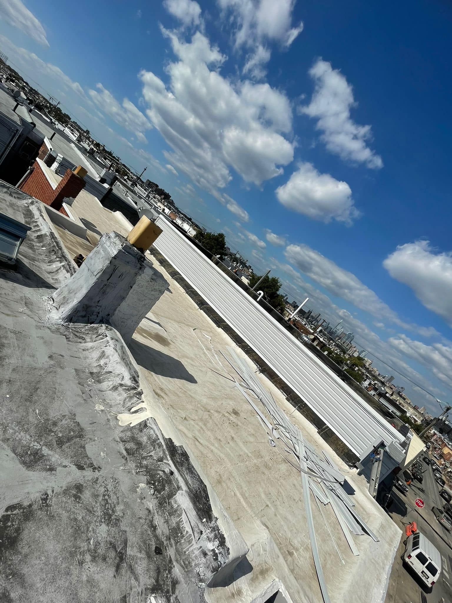 Rooftop view of a building with blue sky and scattered clouds overhead, with a structure being repaired.