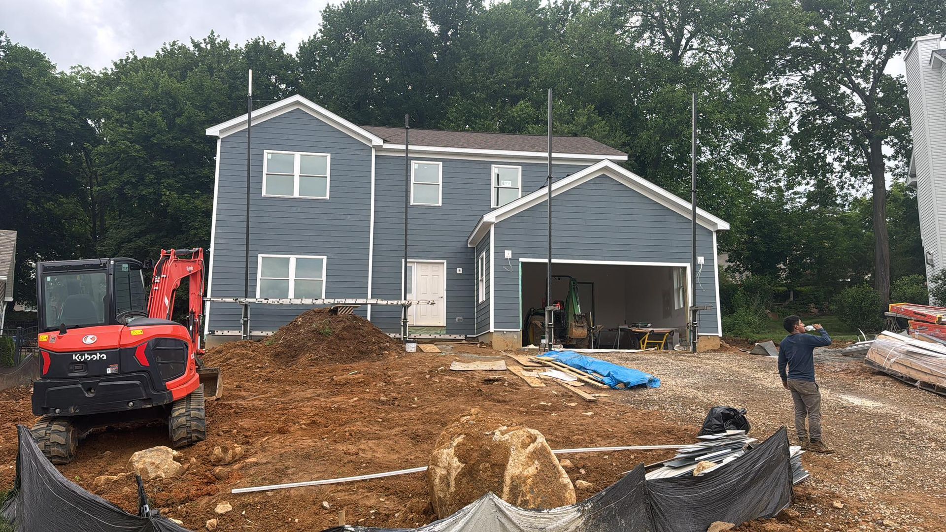 House under construction with excavator, man, and exposed dirt.