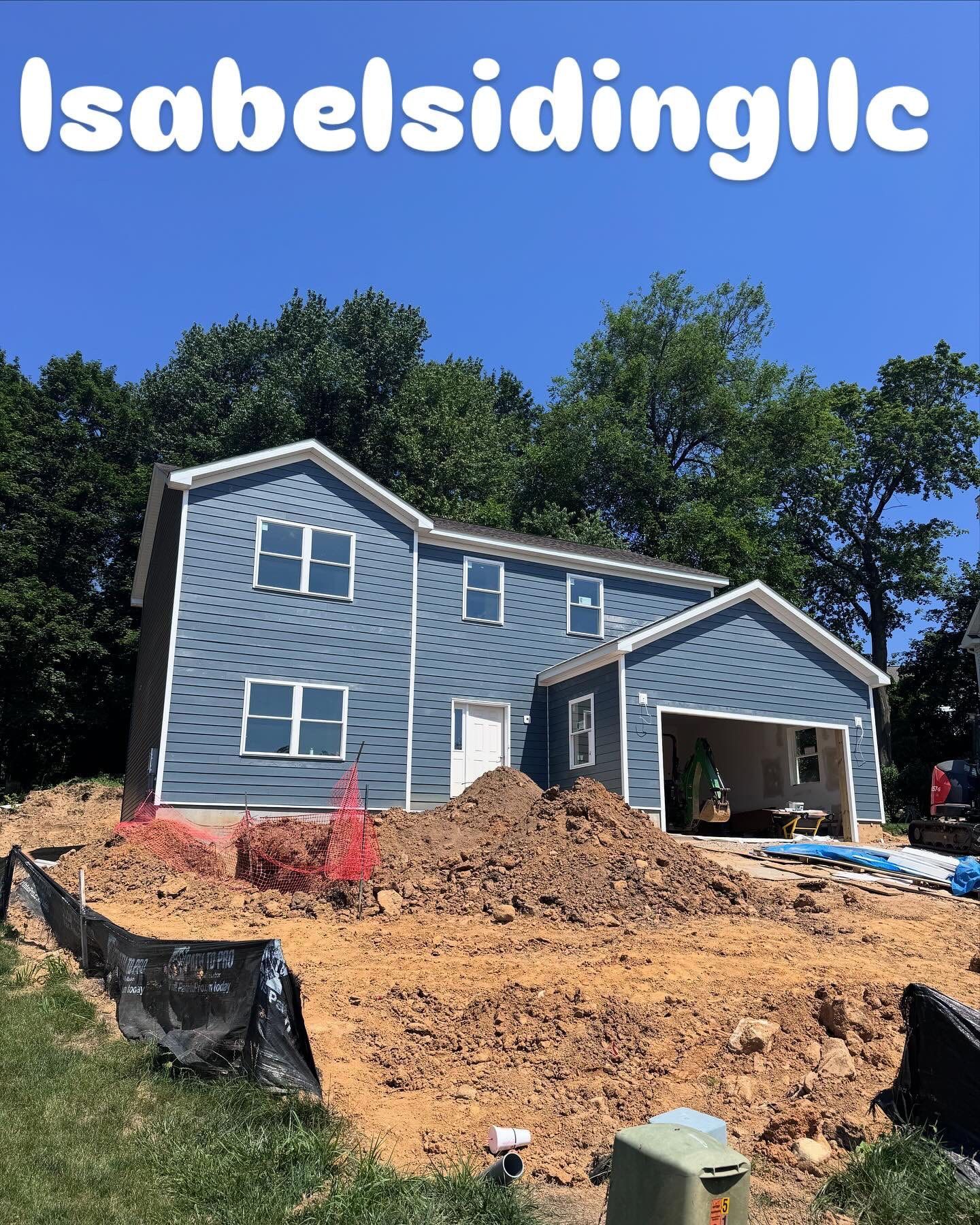Blue-sided house under construction with a garage. Brown dirt surrounds the house. 