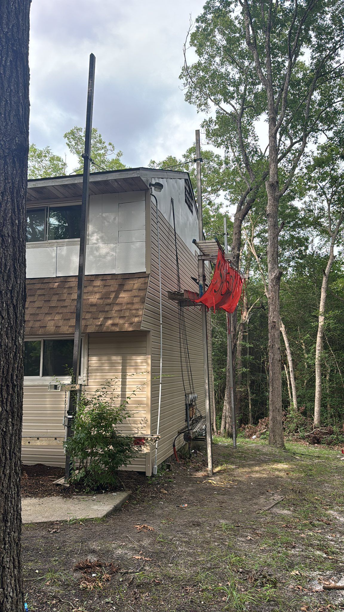 Two-story building with peeling siding among trees, a red bird feeder hangs on the side.