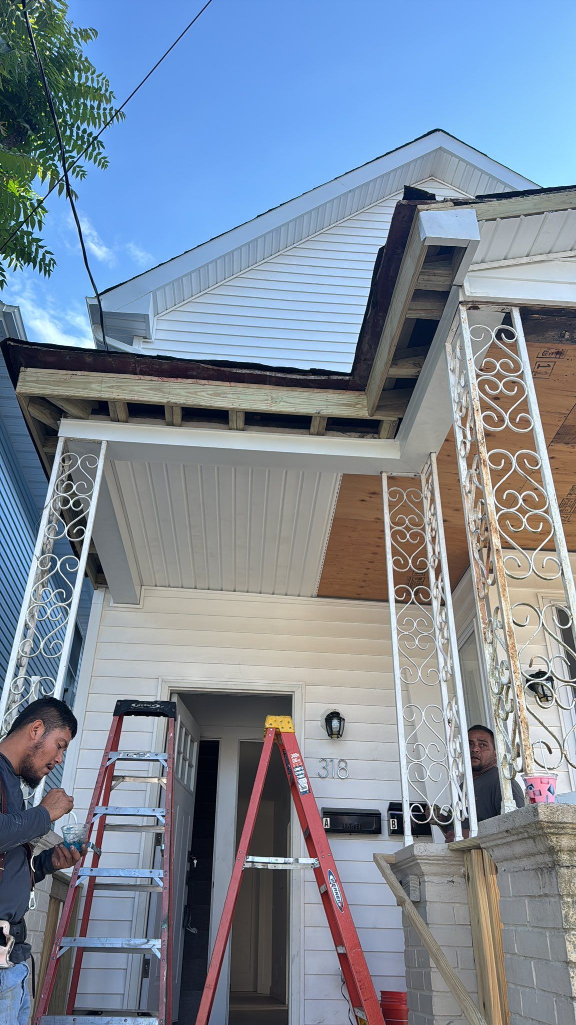 Men working on the front porch of a white house, with ladders and construction materials.