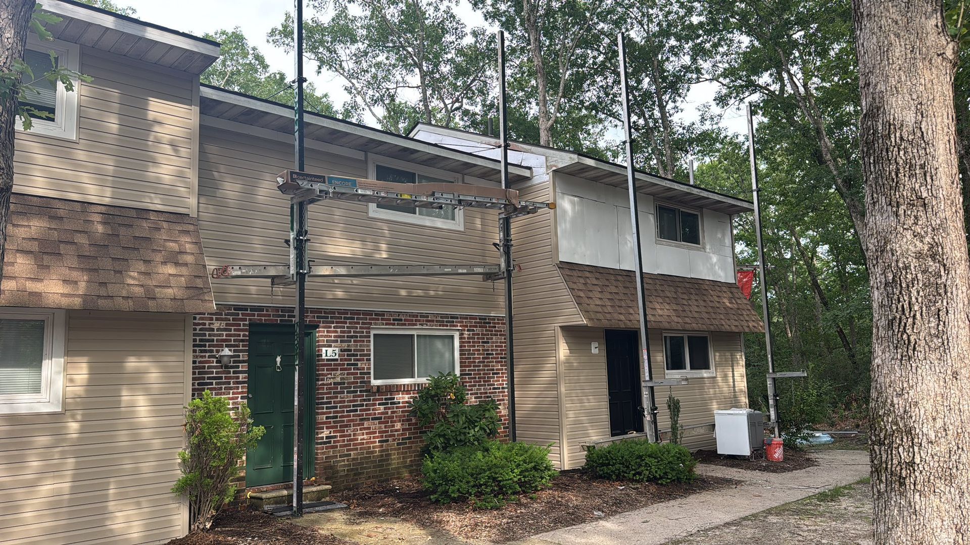 Townhouse with scaffolding; exterior renovation. Beige siding, brick accents, trees.