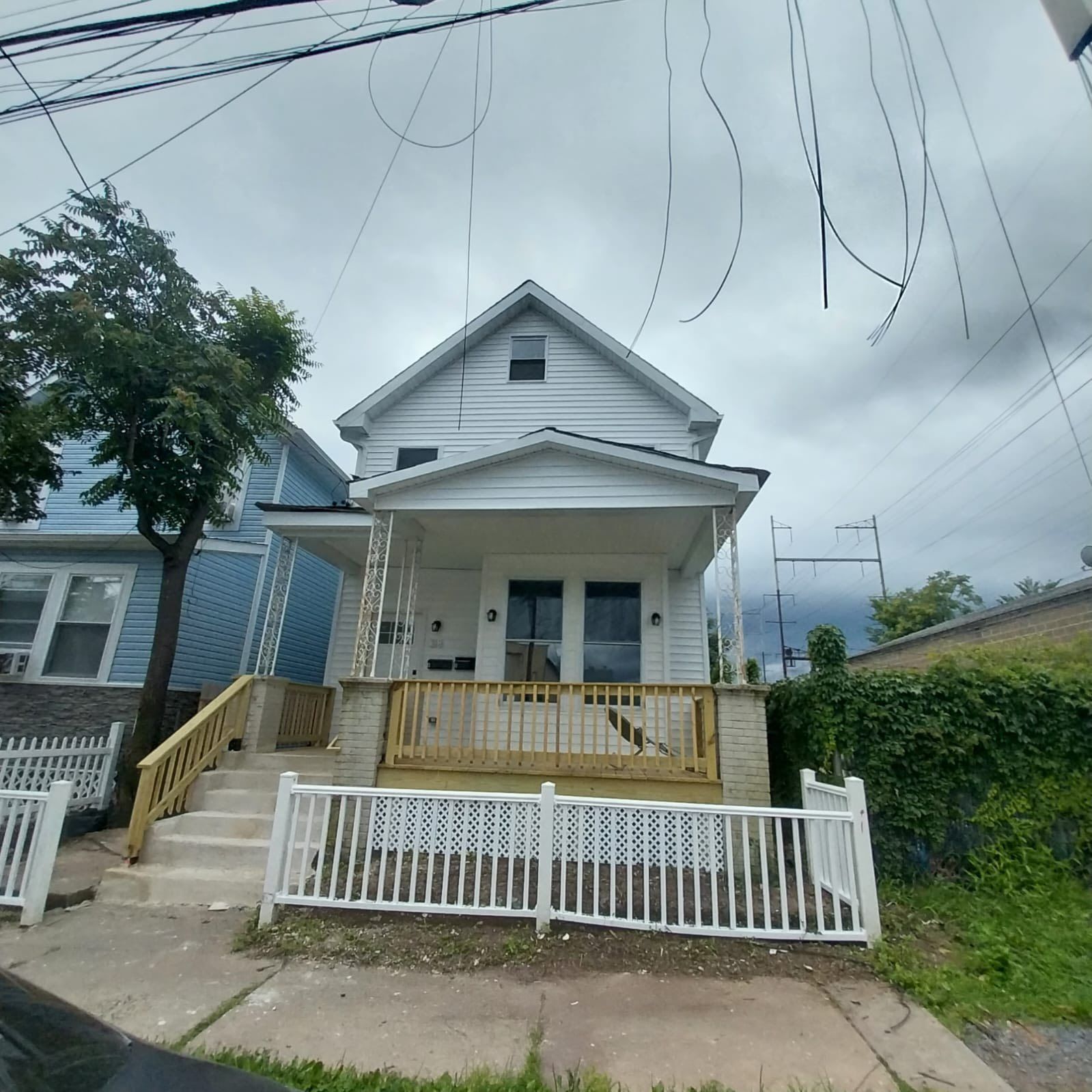 White two-story house with a porch and white picket fence; cloudy sky overhead.
