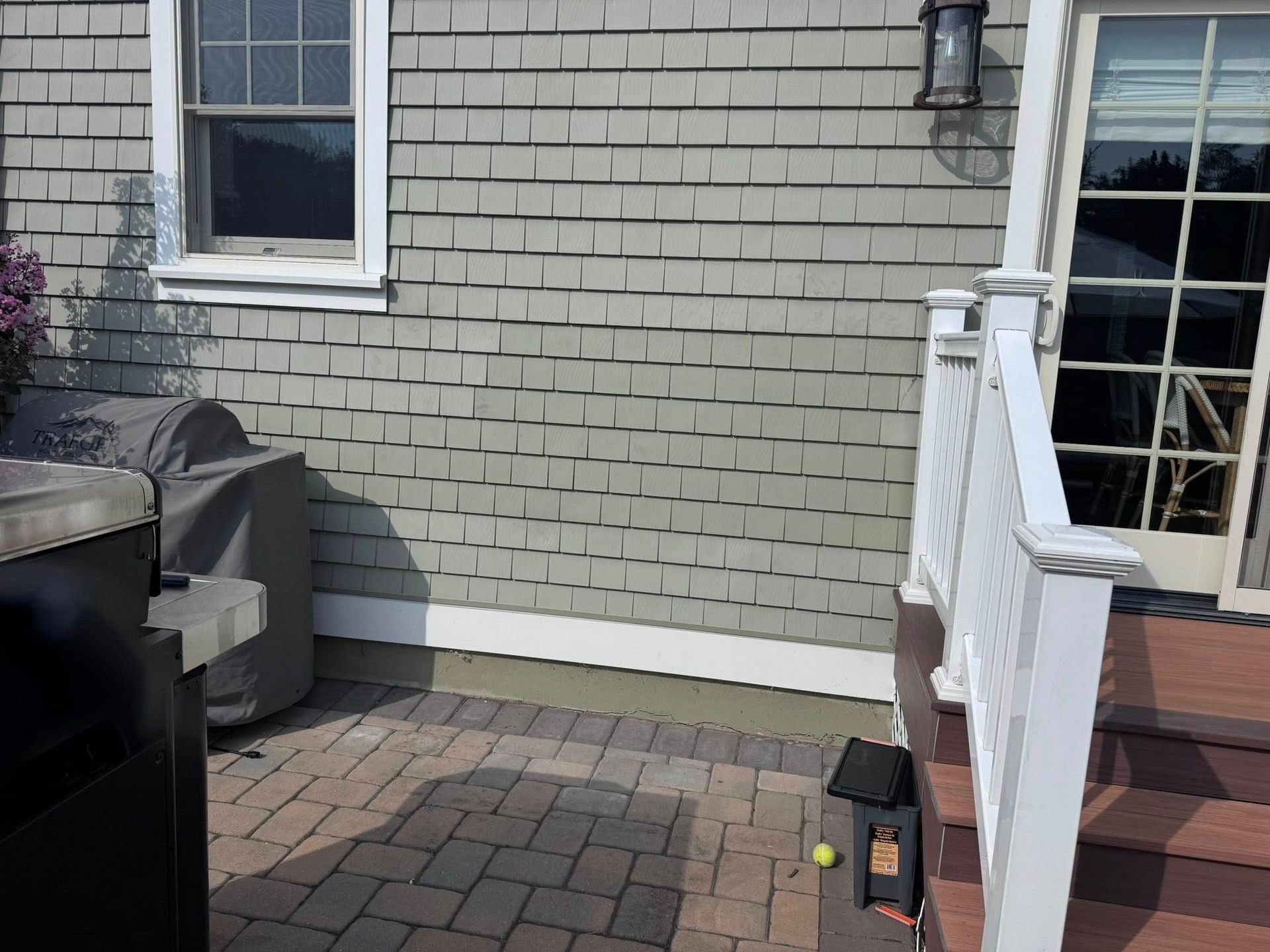 Patio with gray siding, window, covered grill, and wooden railing.