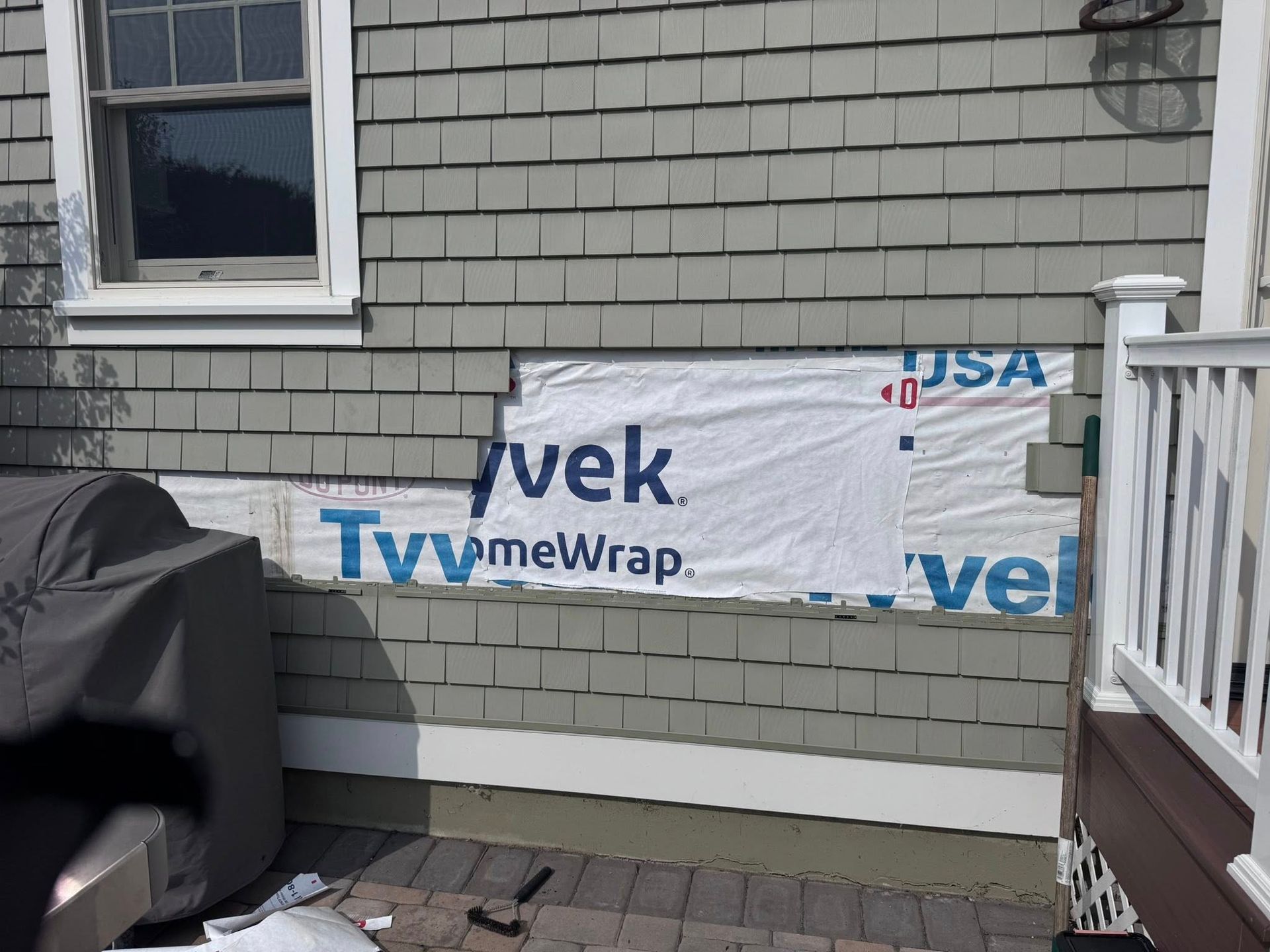 House siding repair with exposed Tyvek wrap, gray shingles, and a window.