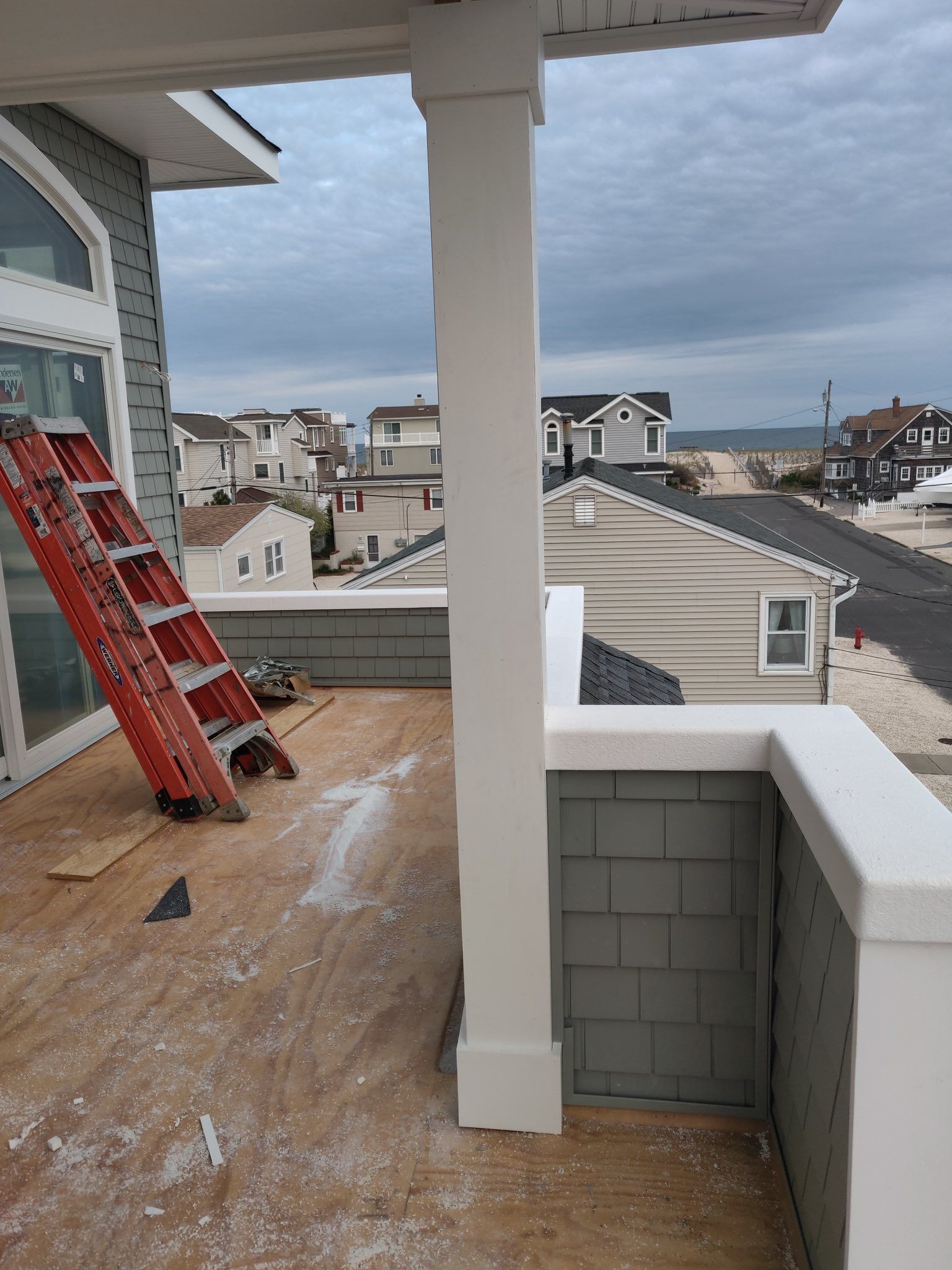 View of a deck under construction with a ladder and houses in the background near the ocean.
