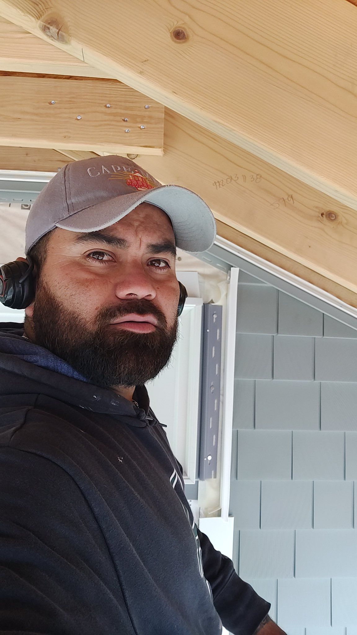 Man wearing a cap and ear protection, working on a construction project, looking at the camera.
