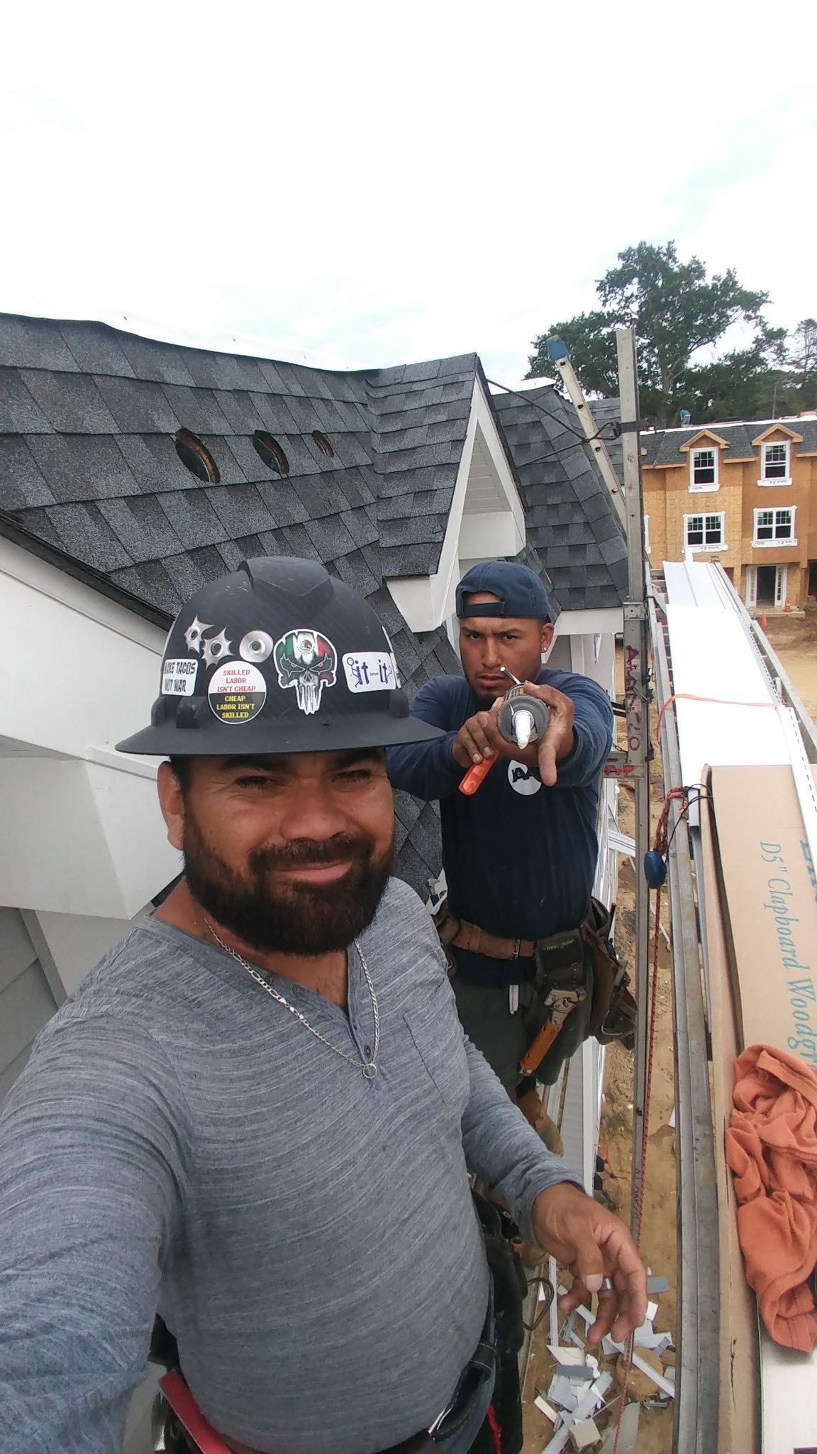 Two construction workers on a roof, one smiling at the camera, the other holding a tool.