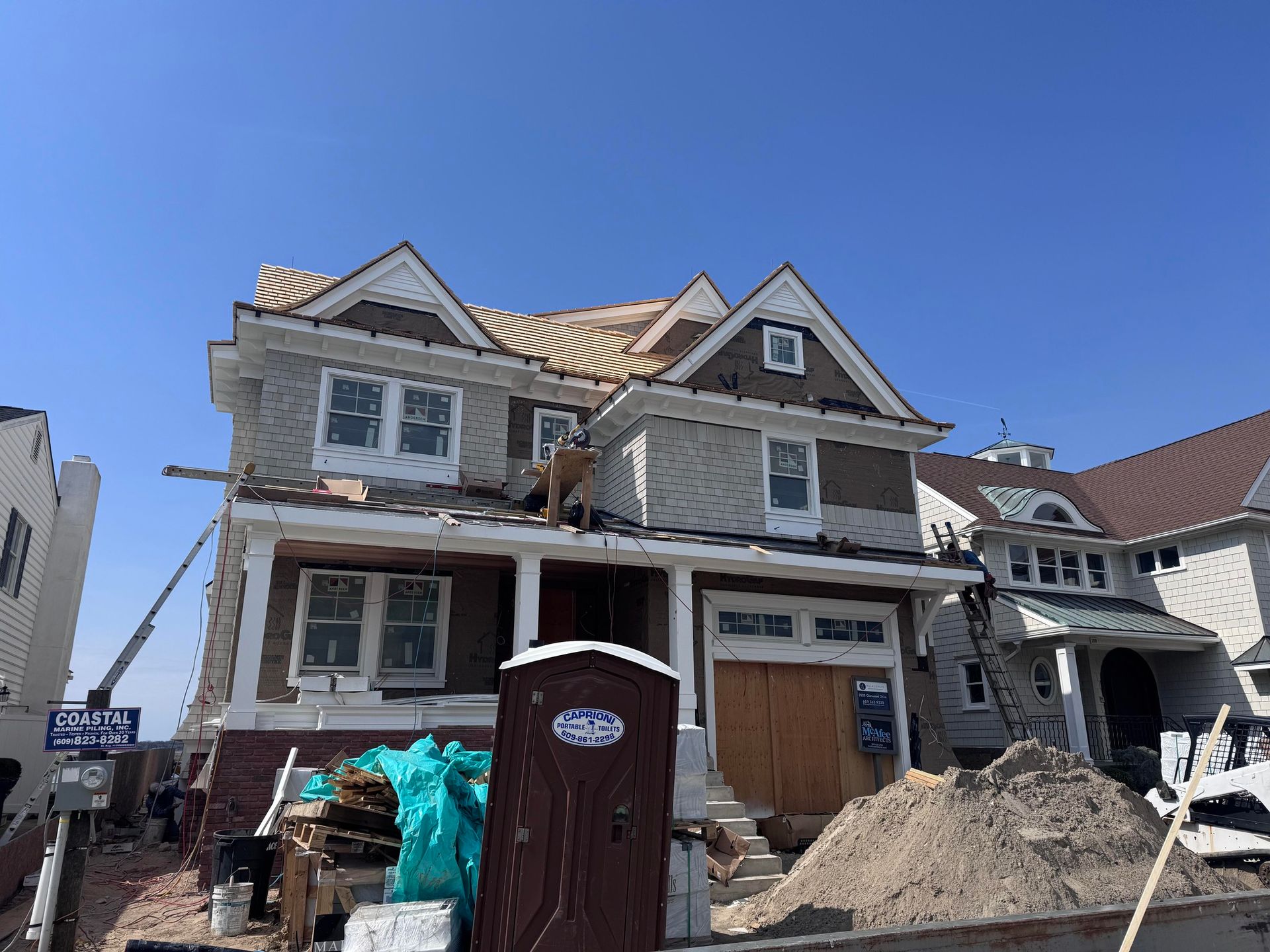 Two-story house under construction; siding partially installed, roof incomplete. Brown and beige exterior, blue sky.