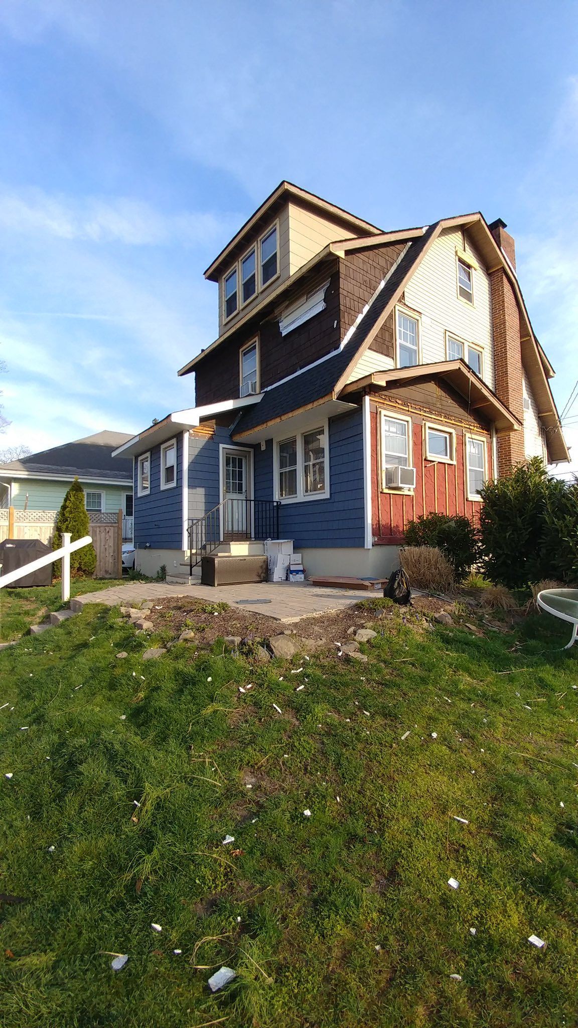 Two-story house with blue siding, tan trim, and a prominent brown curved roof against a blue sky.