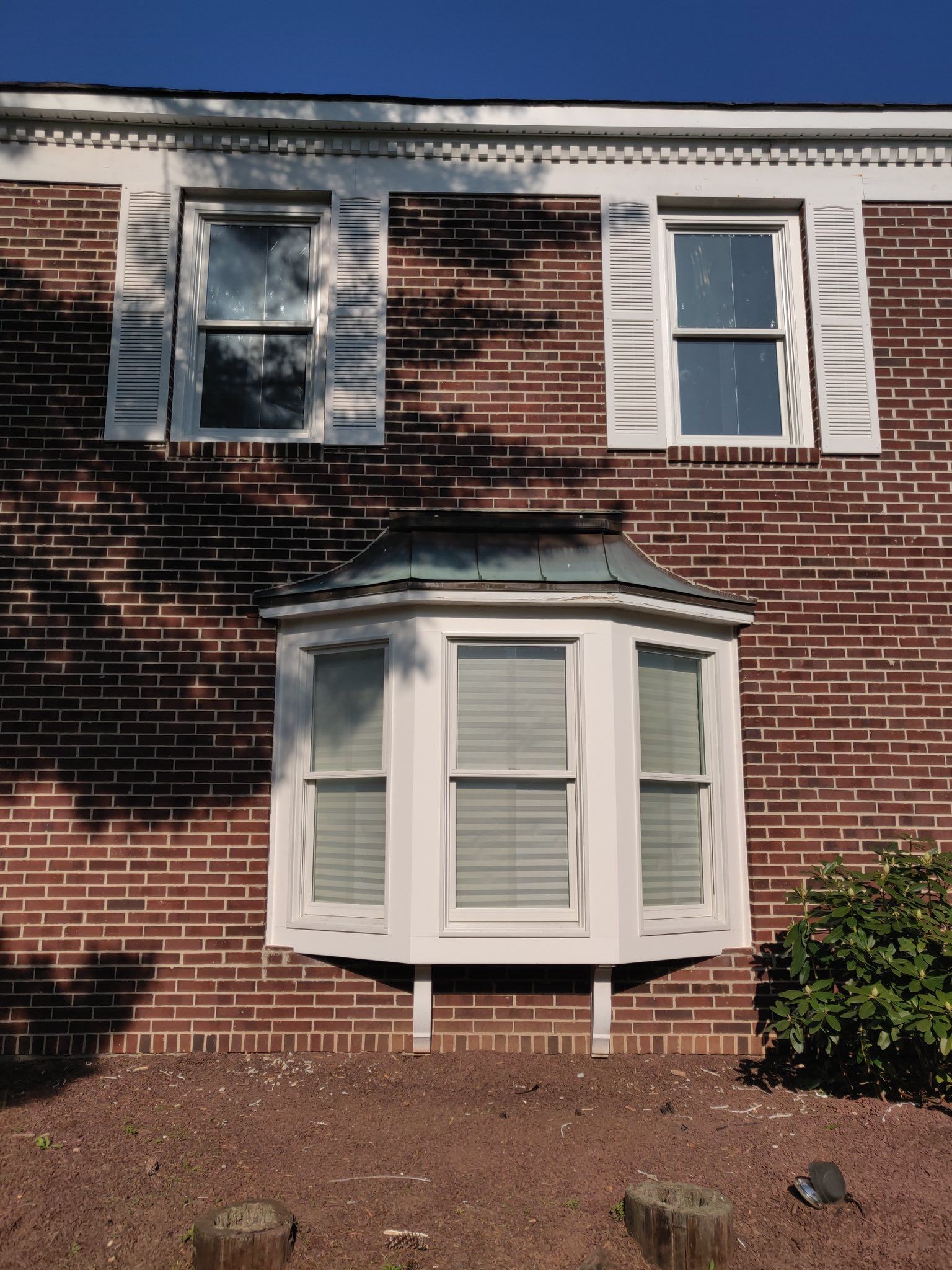 Brick building with white windows and shutters. A bay window sits below two rectangular windows.