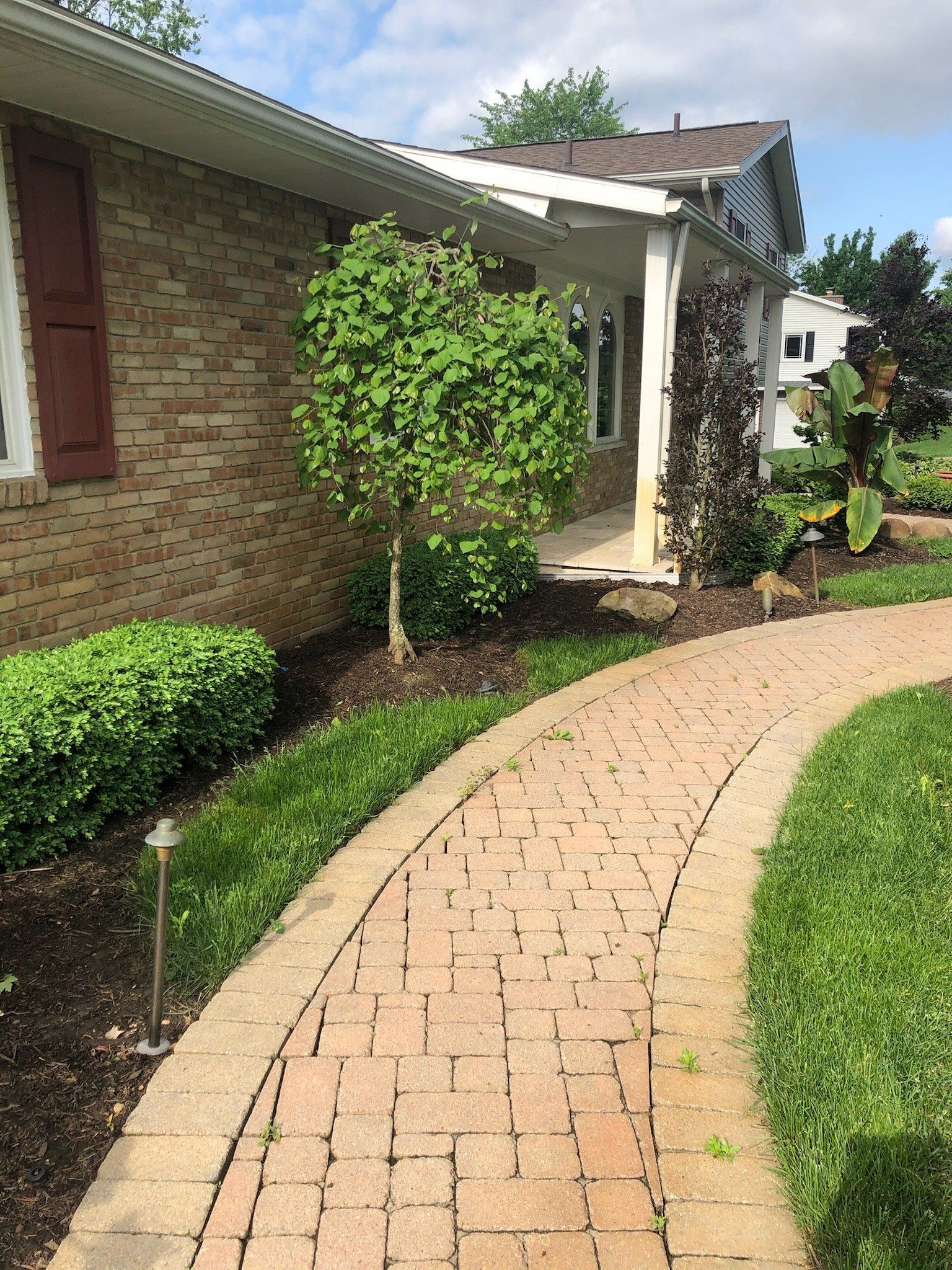 A brick walkway leading to a house with a porch.