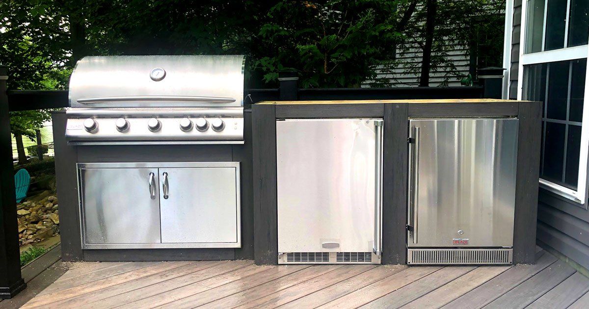 A stainless steel grill and refrigerator are on a wooden deck.