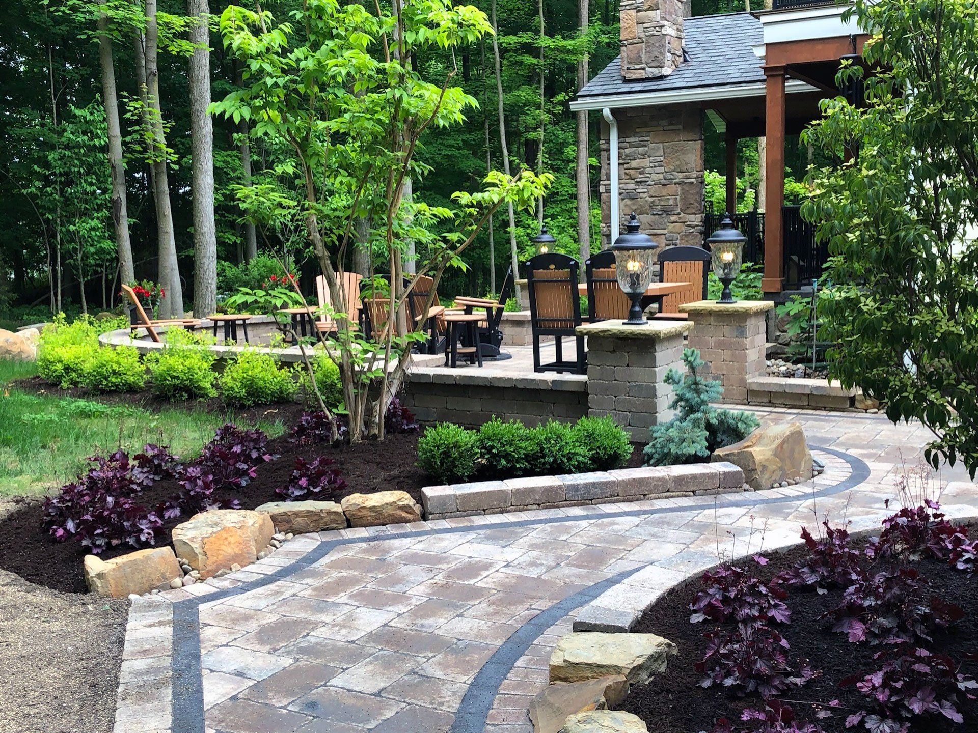 A patio with a fireplace and chairs in a backyard surrounded by trees.