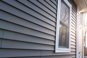 Gray house siding with a white-framed window beside an exterior doorway in bright sunlight