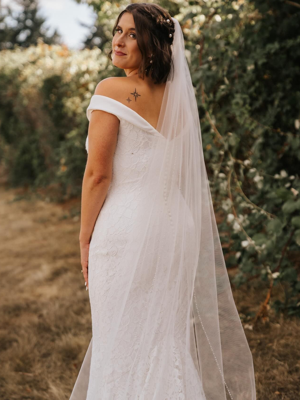 Bride in white wedding dress with veil on stone steps, holding bouquet.
