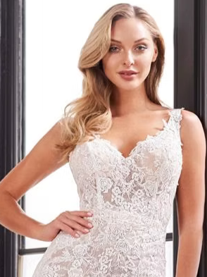 Woman in a white lace wedding dress, leaning against a window, smiling.