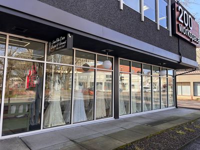 Exterior of a bridal shop with dresses displayed in windows. Building is gray and white.