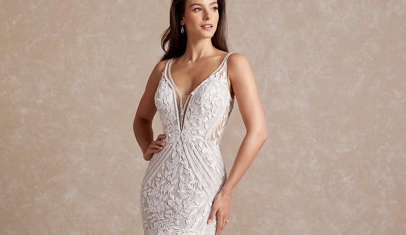 Woman in a white lace wedding dress with a deep V-neckline, hands on hip, looking to the side.