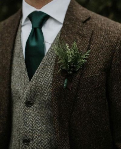 Man in brown tweed suit, gray vest, white shirt, and green tie, with a boutonniere.