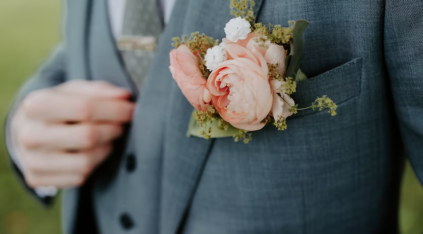 Man's blue suit with a pink flower boutonniere in pocket; hand adjusting the jacket.