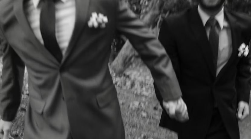 Two men in suits walking outside. One has a boutonniere, they appear to be moving quickly.