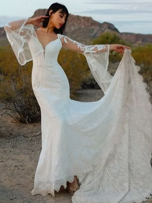 Woman in white wedding dress with lace sleeves and train, posing in desert landscape.