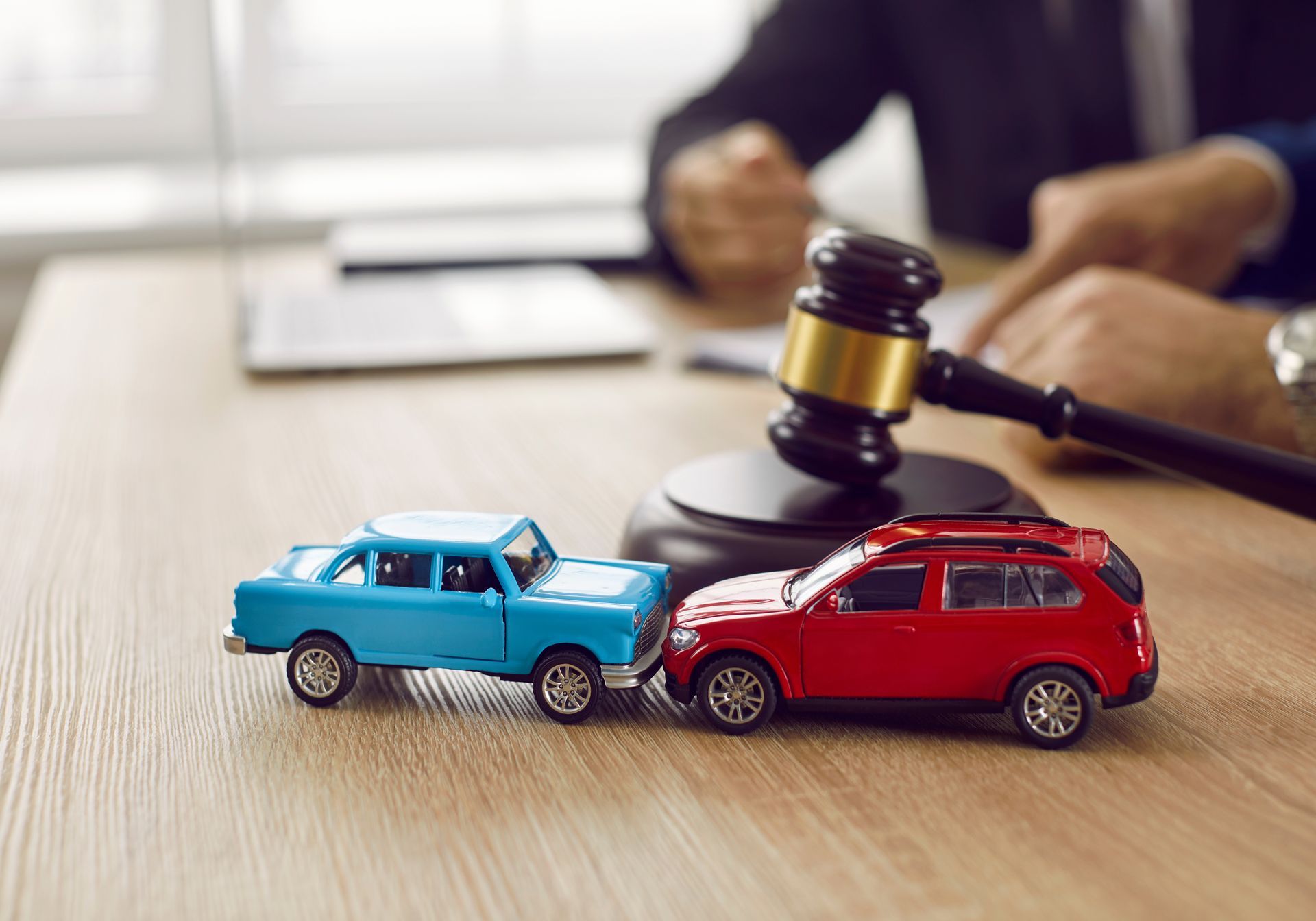 Little crashed blue and red autos on a car crash lawyer's table, next to a wooden gavel.