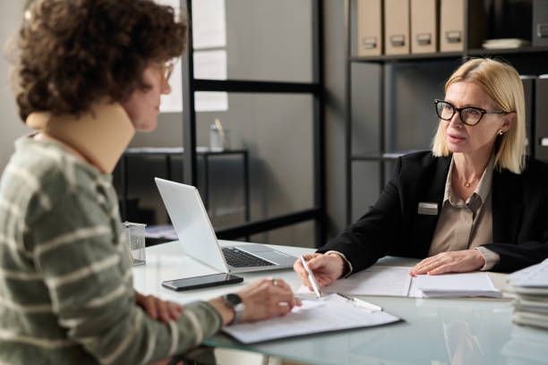 Image of an injured client and her lawyer discussing at a desk with documents and a laptop.
