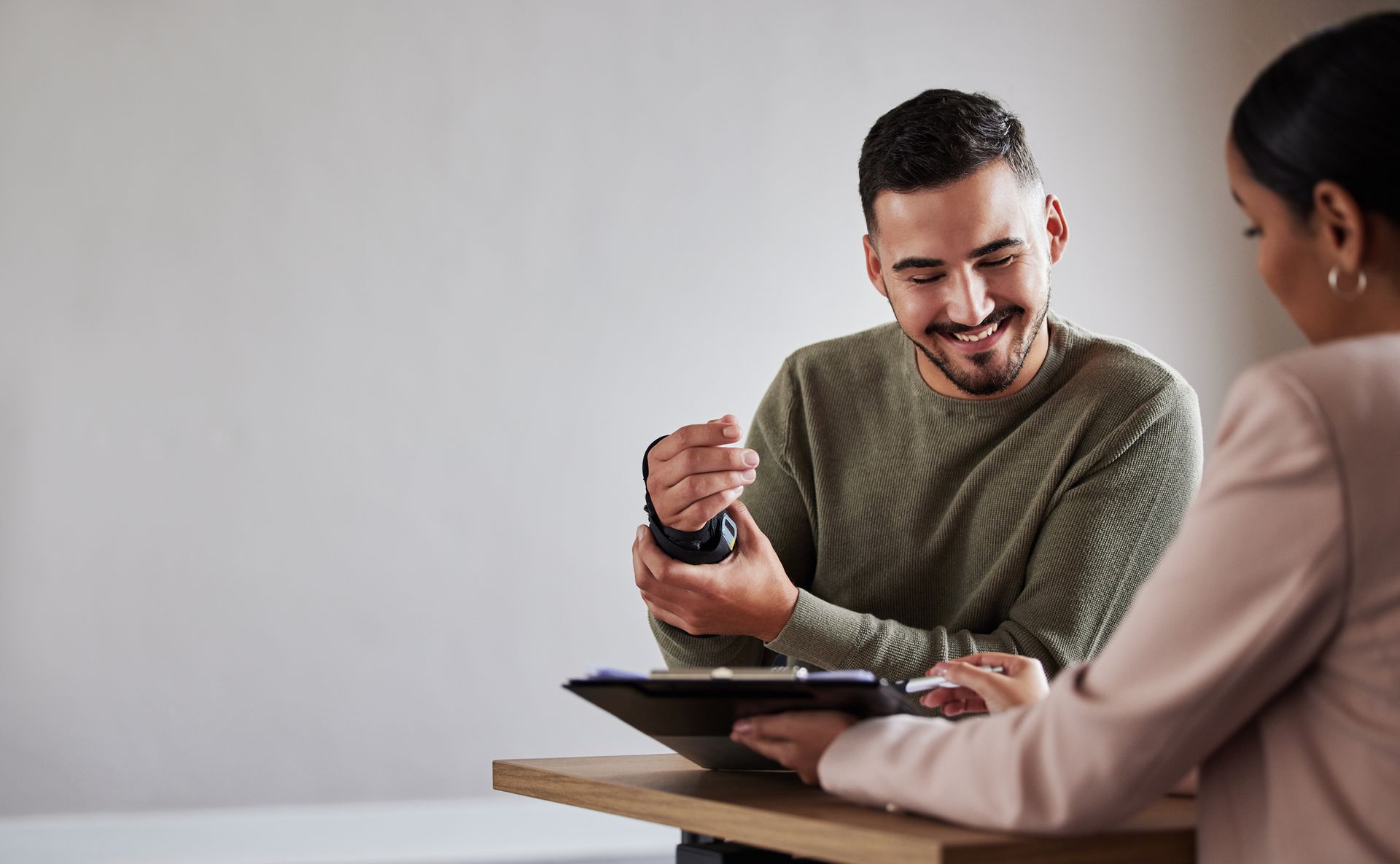 Wide view image of an injured male client holding a wrist brace at a table and his lawyer.