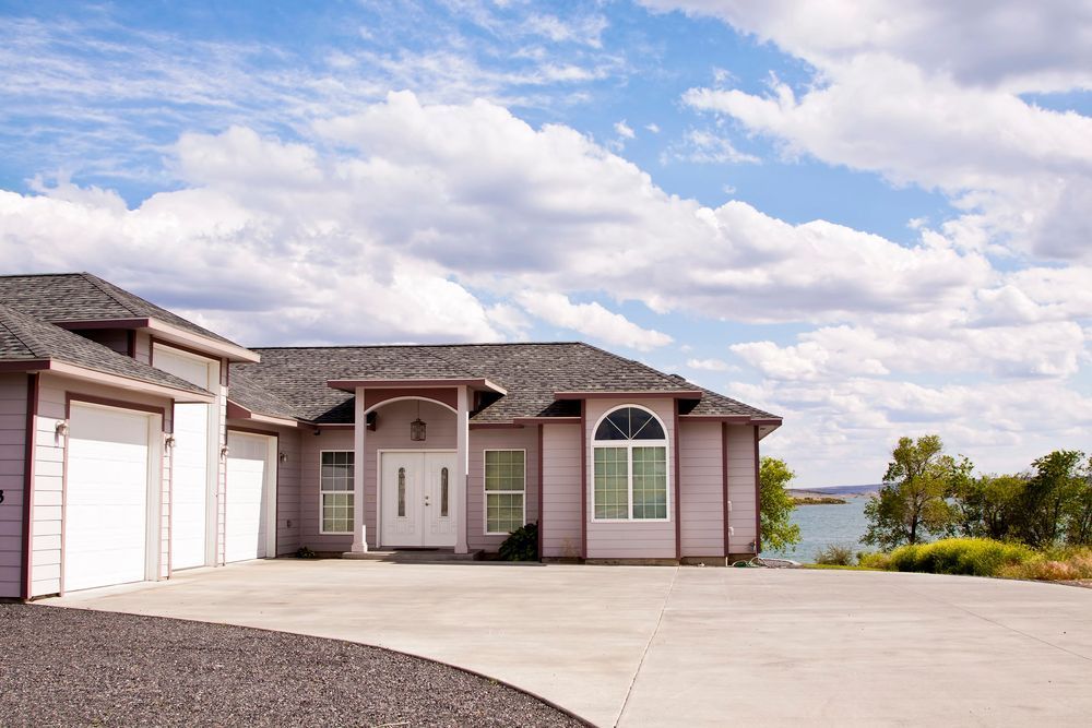 Modern single-story house with a large driveway, garage, and lake view under a partly cloudy sky