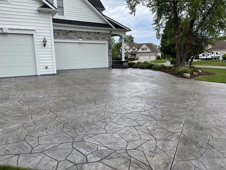 Wet stamped-concrete driveway beside a white garage and front yard trees