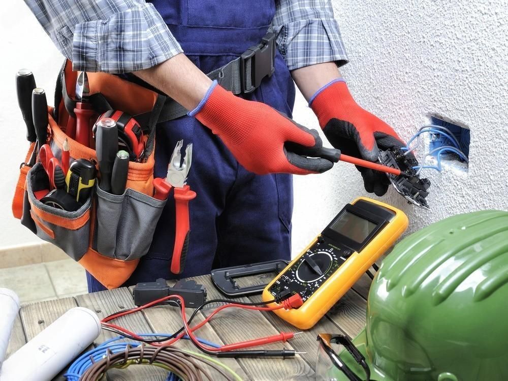 Electrician working on an electrical outlet, wearing gloves and tool belt.